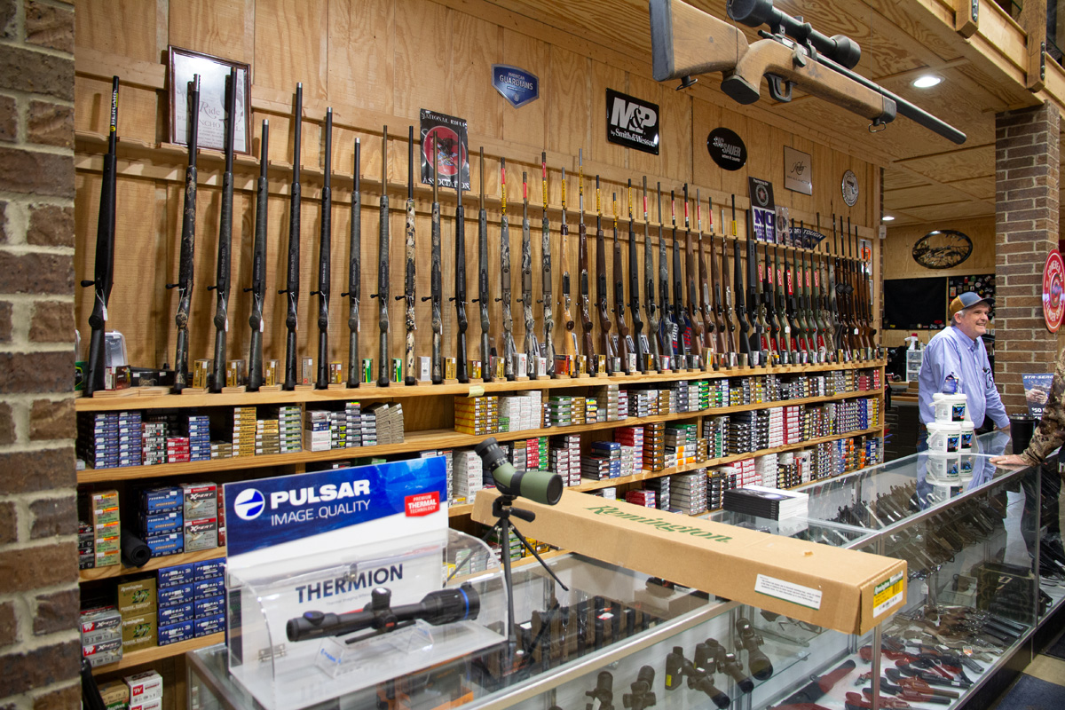 Various handguns and long guns are seen on display.